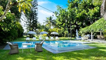 A swimming pool surrounded by lush greenery, outdoor seating, and umbrellas.