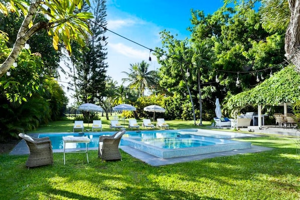 Une piscine entourée d’une végétation luxuriante, avec des espaces de détente en plein air et des parasols.