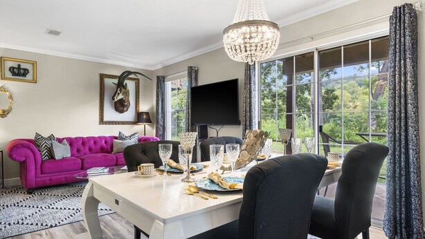 Un coin repas avec une table dressée pour quatre personnes, un lustre et une grande fenêtre agrémentée de rideaux.