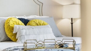 Un lit bien fait, agrémenté d’oreillers à rayures, d’un plaid blanc et d’un plateau sur lequel repose une télécommande.