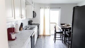 A modern kitchen with white cabinets, a marble countertop, a coffee maker, and a dining area with a table and chairs.