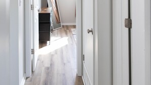 A hallway with wooden flooring, white walls, and a ceiling light fixture.