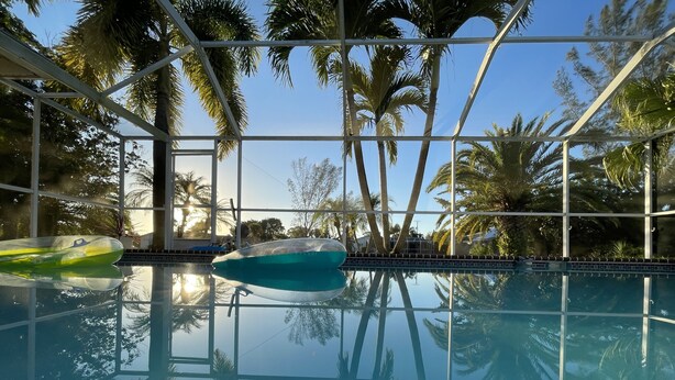 An indoor swimming pool with clear glass walls, surrounded by palm trees and a view of the sky.