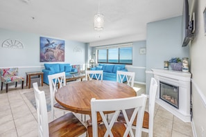 A spacious living room with a wooden dining table, blue sofas, and a fireplace. - Stunning View Direct Oceanfront Clean 2BR-Indoor/Outdoor Pools and Lazy River (Myrtle Beach)
