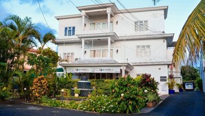 A two-story building with a white facade, multiple balconies, and a landscaped front yard with tropical plants. - Super spacious (Quatre Bornes)