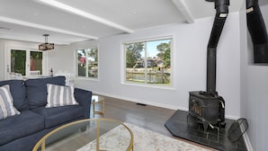 A modern living room with a dark blue sofa, a round glass coffee table, and a black wood-burning stove. - Waterfront Property E. Quogue Minutes From The Hamptons (East Quogue)