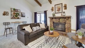 A cozy living room with a brown leather sofa, a coffee table, a fireplace, and a ceiling fan. - Forest-View Balcony: Pinetop-Lakeside Condo (Pinetop-Lakeside)