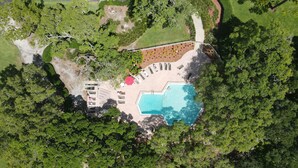 An aerial view of a resort with a swimming pool, sun loungers, and a covered area with a red umbrella.