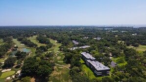 An aerial view of a golf course with multiple bunkers, water hazards, and a large building complex in the foreground.