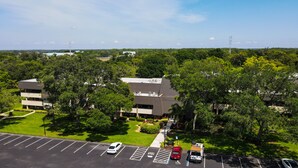 An aerial view of a building complex surrounded by lush greenery, with a parking lot in the foreground.