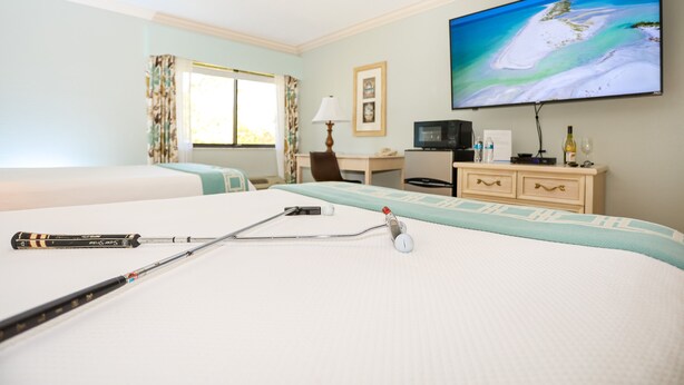 A hotel room with two beds, a desk with a computer, a TV on the wall, and a bedside table with a lamp and a bottle.