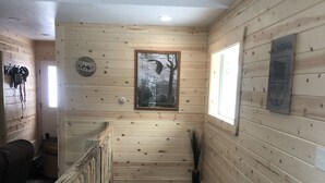 A wooden interior with a staircase leading to a lower level, a framed picture on the wall, and a sign with 'MONTANA' on it. - Beautiful Cabin located in the Little Belt Mountains (White Sulphur Springs)