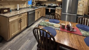 A modern kitchen with wooden cabinets, stainless steel appliances, and a dining area with a wooden table and chairs. - Beautiful Cabin located in the Little Belt Mountains (White Sulphur Springs)