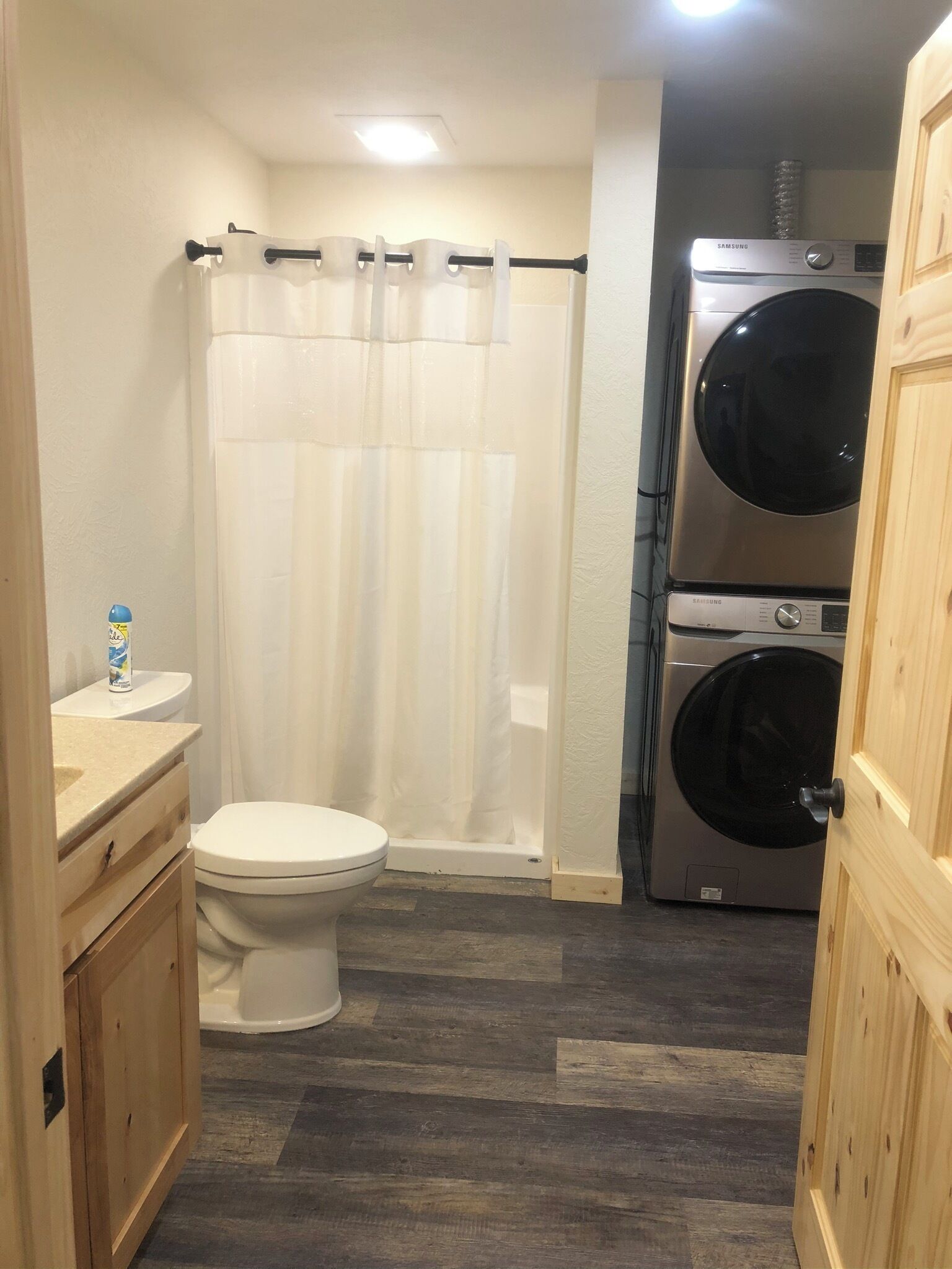 Een kleine badkamer met toilet, douchegordijn en een gestapelde wasmachine en droger.