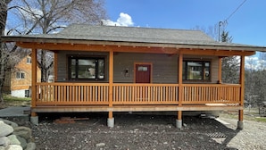 A two-story wooden cabin with a porch, large windows, and a red door. - Private mountain view haven in the beautiful West Kootenays (Kaslo)