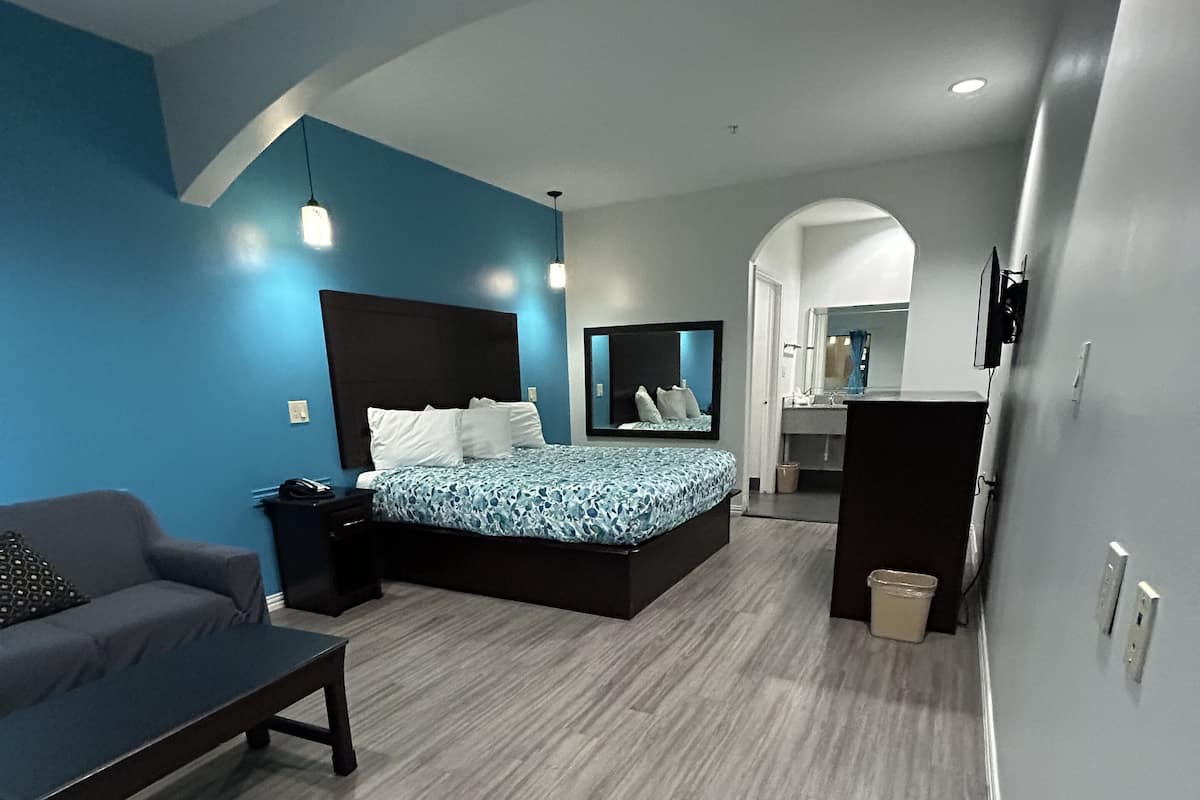 A modern bedroom with a bed, a sofa, a desk, and a mirror.
