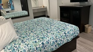 A bedroom with a bed, a TV, a mirror, and a small desk. - Regency Inn and Suites (Humble)