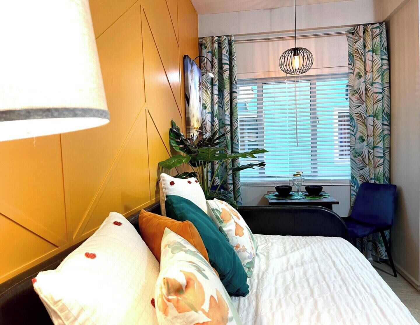 Une chambre d’hôtel avec un lit, une petite table sur laquelle se trouve une plante, une chaise et une fenêtre avec des rideaux.