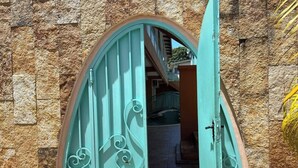 A turquoise arched entrance with decorative metalwork, leading to a staircase and a building with stone walls.