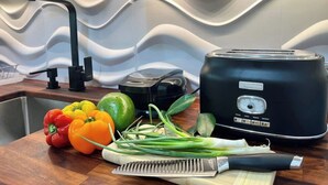 A kitchen with a modern design, featuring a black toaster, a sink, and a variety of fresh vegetables on the counter.