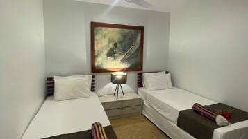 A hotel room with two single beds, a ceiling fan, a nightstand with a lamp, and a painting on the wall.