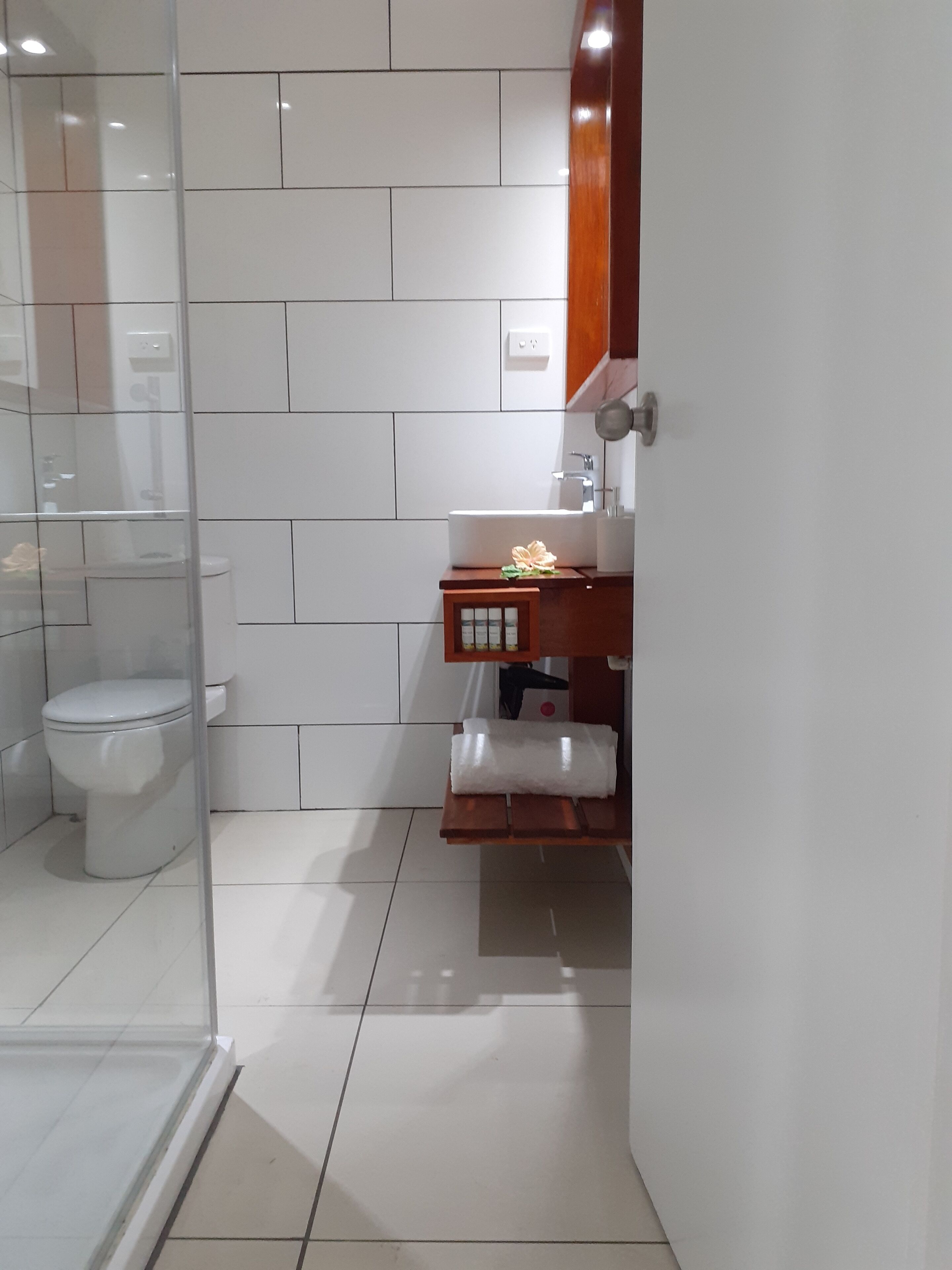 A modern bathroom with a glass shower enclosure, a white toilet, and a wooden vanity with a sink and mirror.