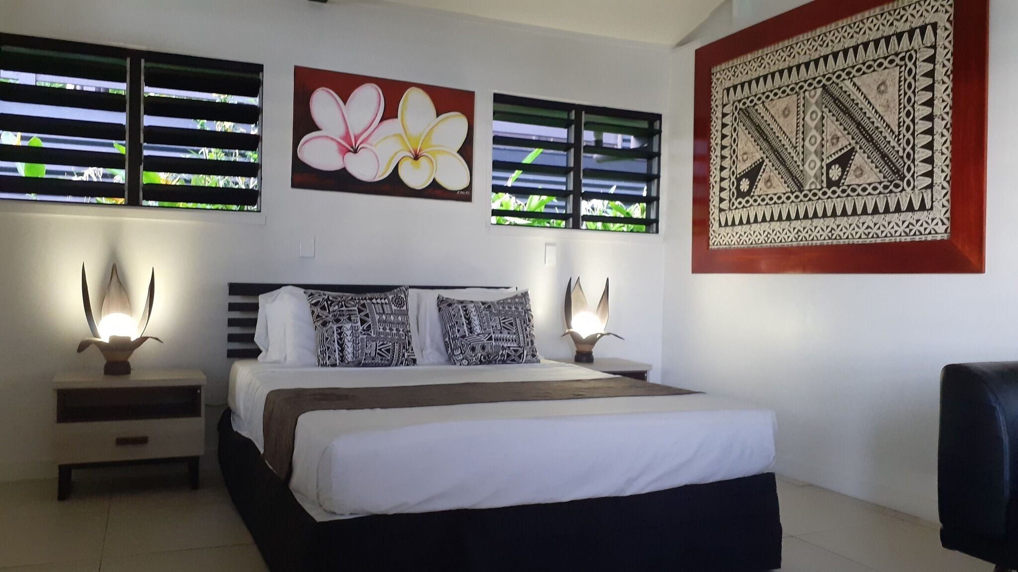 A bedroom with a bed, two bedside tables, a nightstand, a chair, and artwork on the walls.