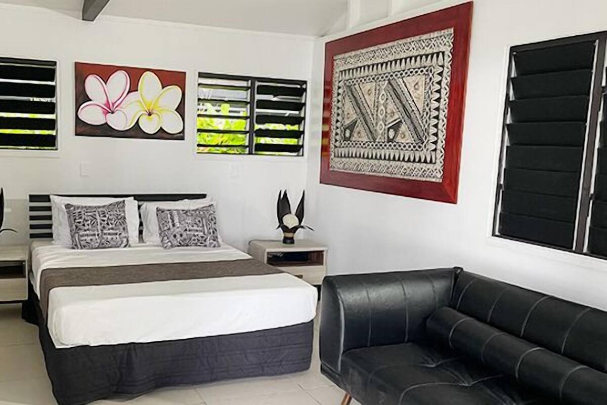 Ein Schlafzimmer mit einem Bett, zwei Nachttischen, einem schwarzen Ledersofa und Kunstwerken an den Wänden.