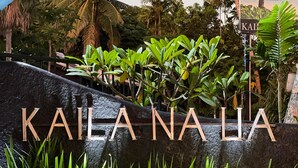 A sign with "KAILA NALIA" written in large letters, surrounded by lush greenery and a stone wall. - Kaila Na Ua Resort (Korotogo)