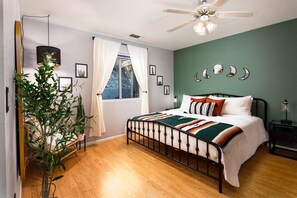 Een slaapkamer met een bed, een plafondventilator, een raam met gordijnen, een plant en spiegelwanden.