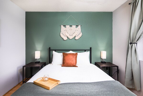 Una cama bien hecha con almohadas blancas y marrones, una bandeja de madera y un adorno en la pared.