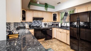 A modern kitchen with wooden cabinets, a black refrigerator, and a granite countertop.