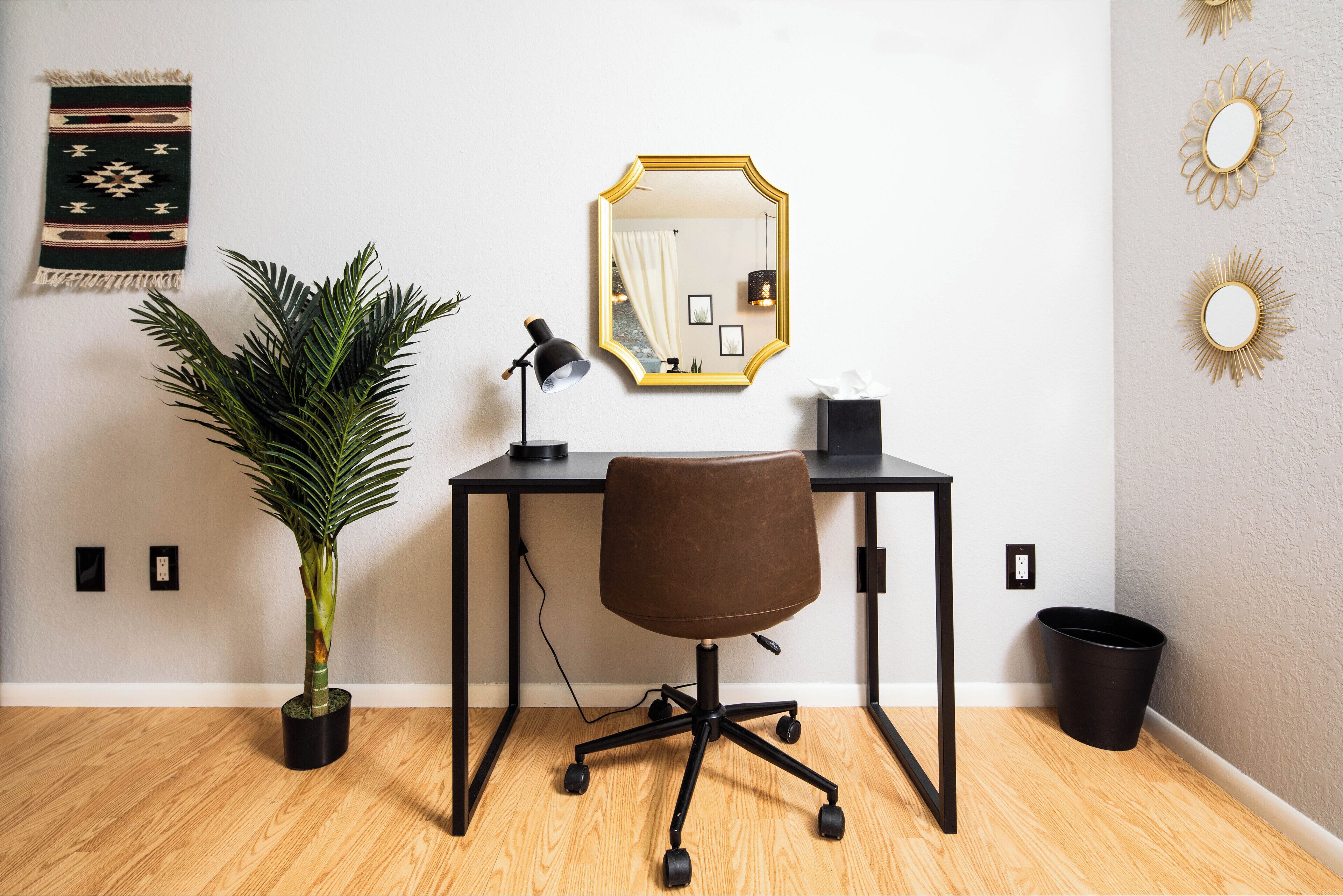 A modern office space with a desk, chair, potted plant, and decorative wall mirrors.