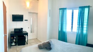 Una habitación de hotel con cama, escritorio con televisor, cafetera y ventana con cortinas.