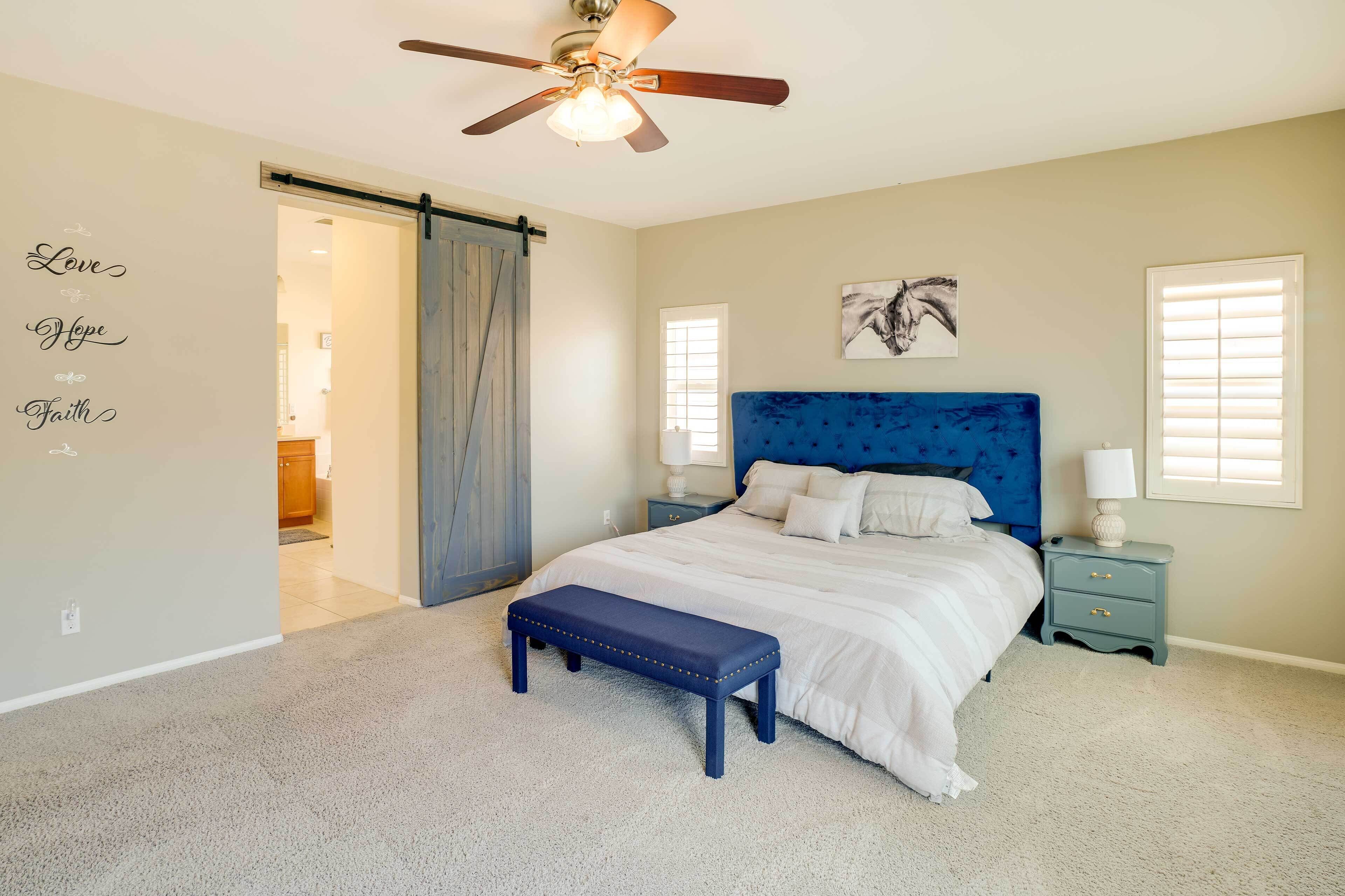 A bedroom with a bed, a bench, a nightstand, a ceiling fan, and a sliding door.