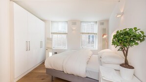 Een moderne slaapkamer met een bed, een witte garderobe, ramen en een potplant.