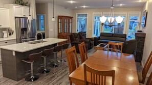 A modern kitchen with a central island, bar stools, a dining table with chairs, a built-in oven, and a refrigerator.