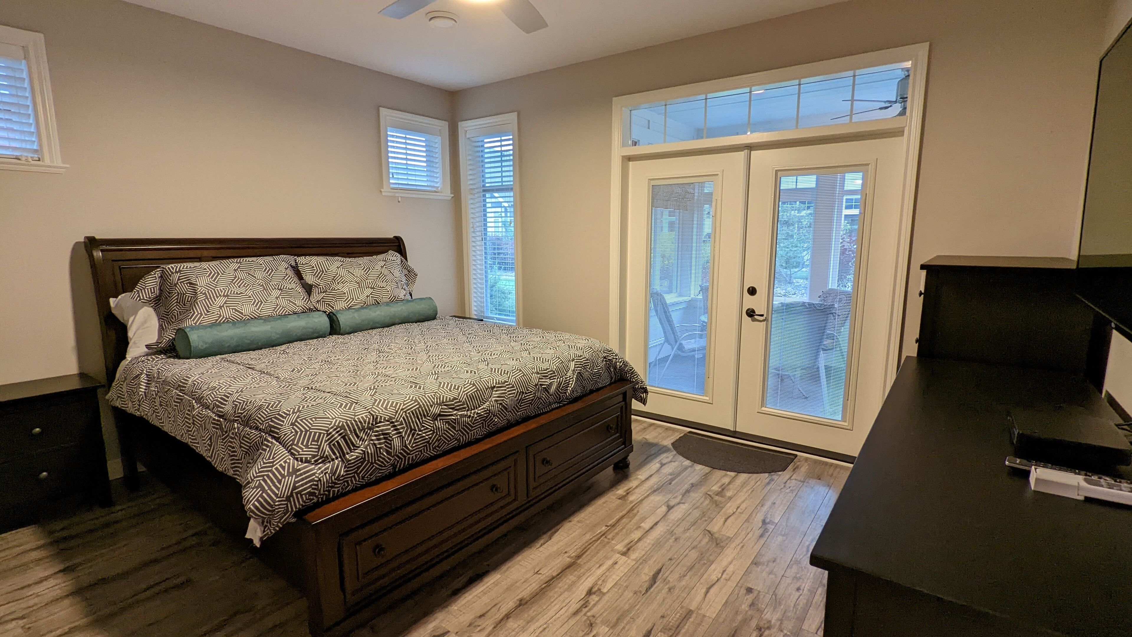 A bedroom with a wooden bed, a desk, and a sliding glass door to the outside.