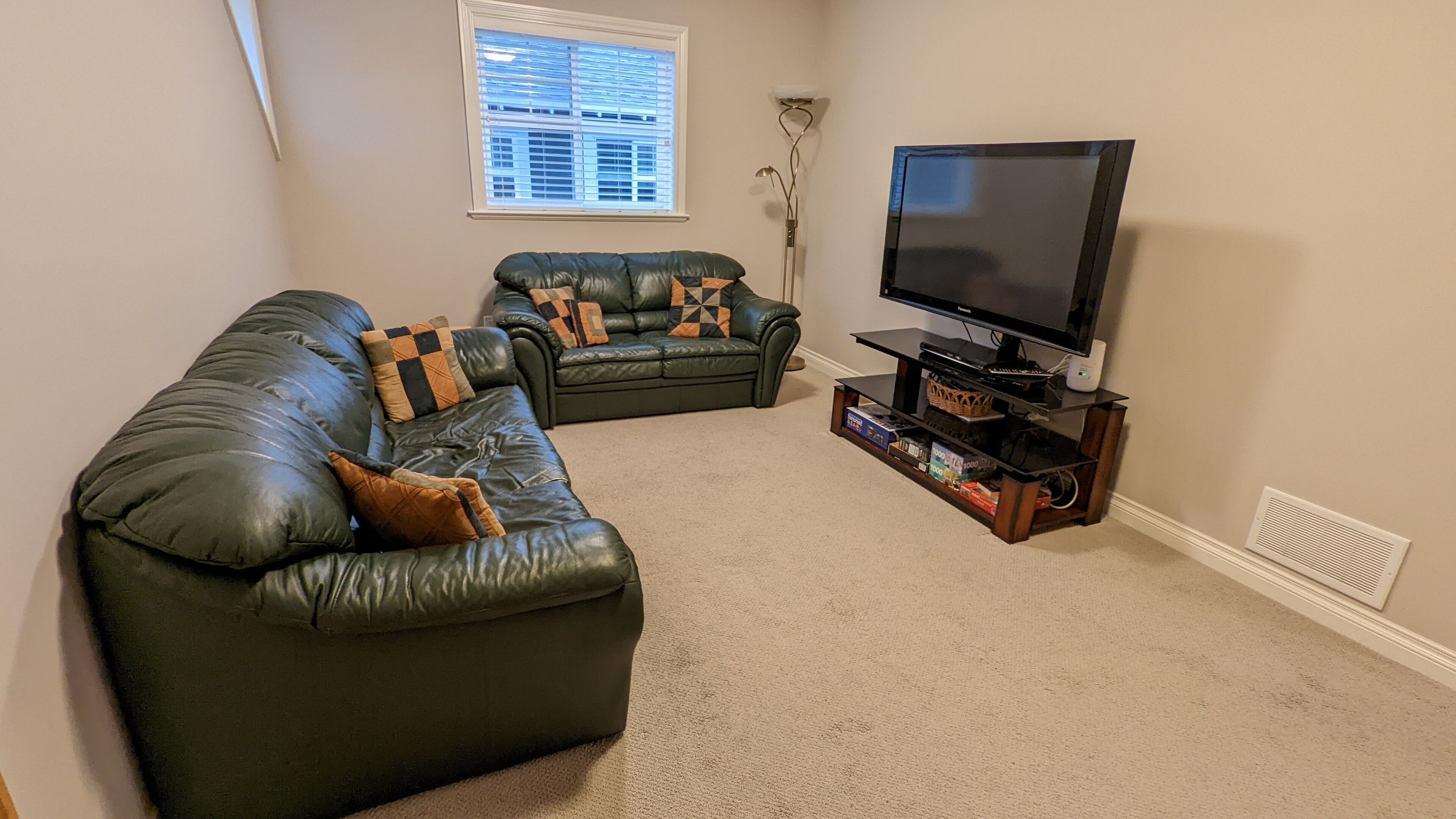 Ein Wohnzimmer mit einer großen Ledersofa, einem kleineren Sofa und einem Flachbildfernseher auf einem Holzständer.