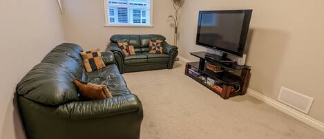Ein Wohnzimmer mit einer großen Ledersofa, einem kleineren Sofa und einem Flachbildfernseher auf einem Holzständer.