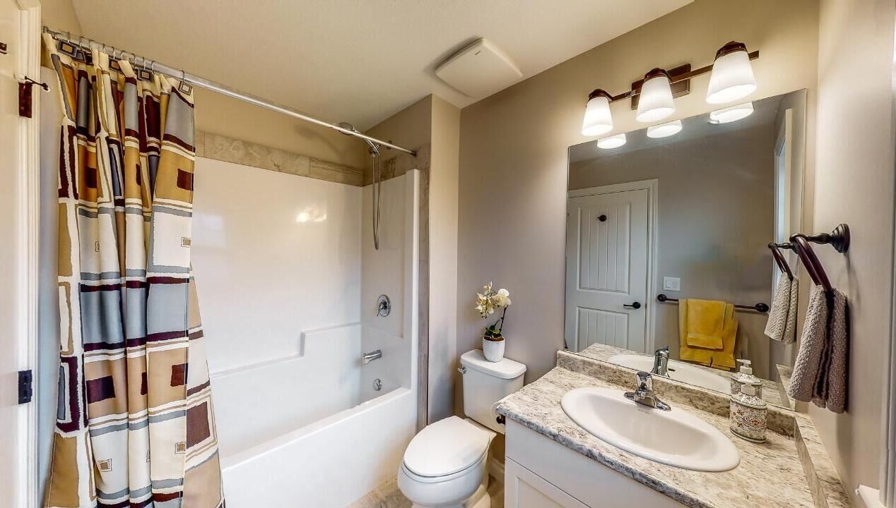 Een badkamer met douche, toilet, wastafel en spiegel.