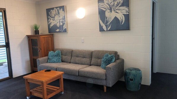 Una sala de estar con un sofá gris, dos almohadas azules, una mesa de centro de madera y dos cuadros florales colgados en la pared.
