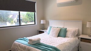 A bedroom with a bed, a nightstand, a lamp, and a window with a view of greenery outside.