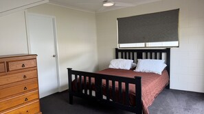 A bedroom with a wooden bed, a dresser, and a window with blinds.