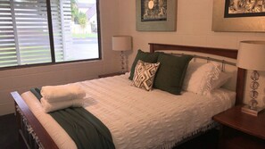 Una cama bien hecha con una manta blanca y verde, dos almohadas y una mesita de noche con una lámpara.