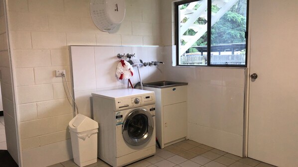 A compact laundry room with a washing machine, a drying rack, and a sink.