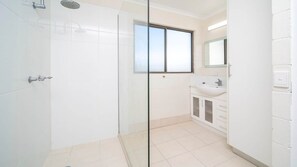 Un baño moderno con cabina de ducha de vidrio, un ventanal grande y un lavamanos blanco con un espejo encima.