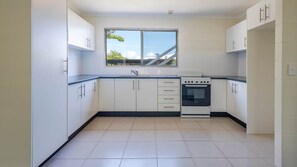 A modern kitchen with white cabinets, a built-in oven, and a window providing a view of the outdoors.