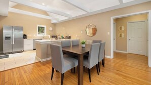 Uma cozinha moderna com uma ilha central, uma área de refeições com mesa e cadeiras, e um corredor que leva a uma porta.