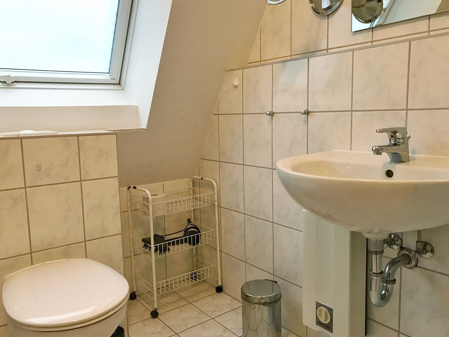 A bathroom with a toilet, a sink, a mirror, and a window.
